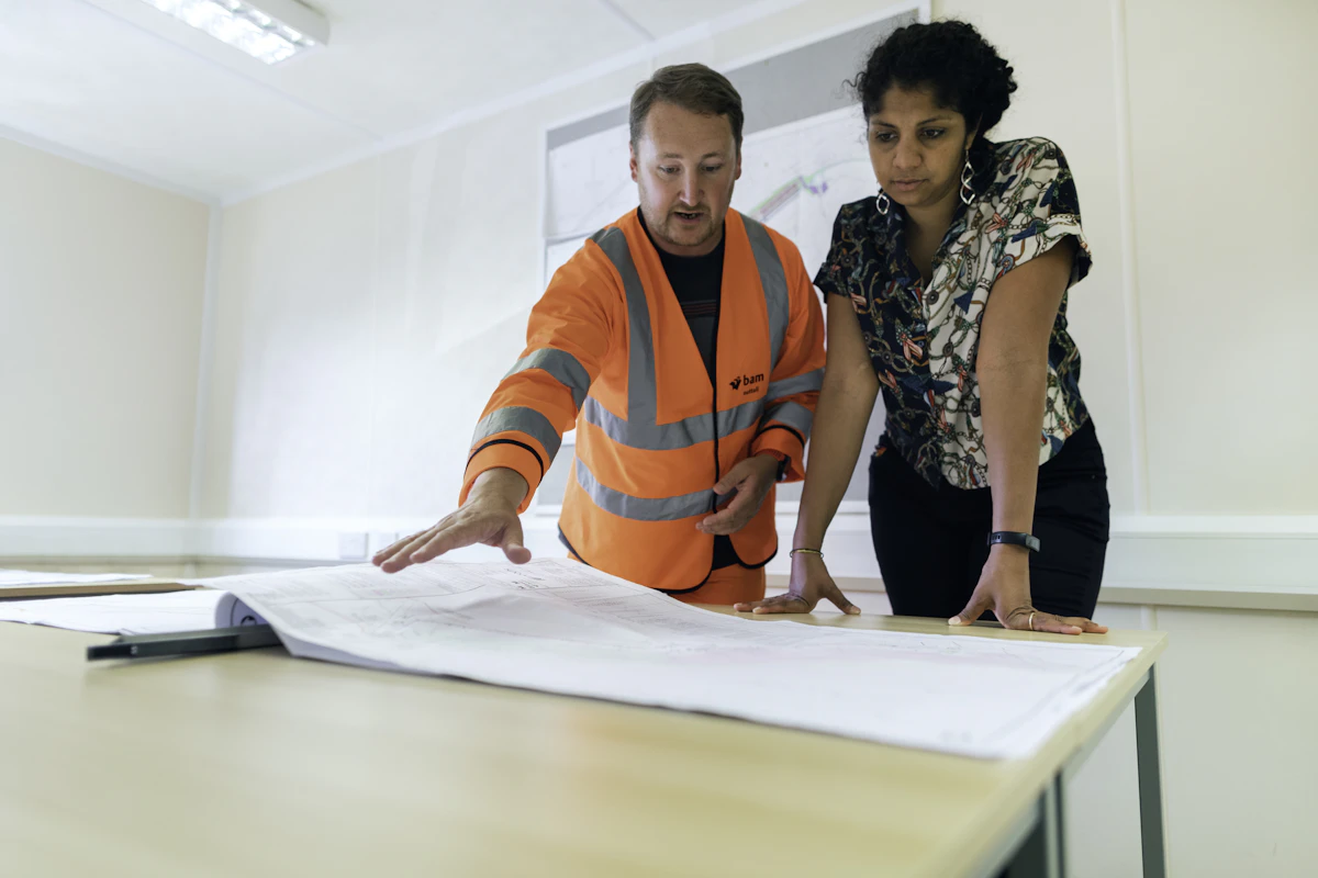 An engineer and a colleague reviewing building plans together at a desk