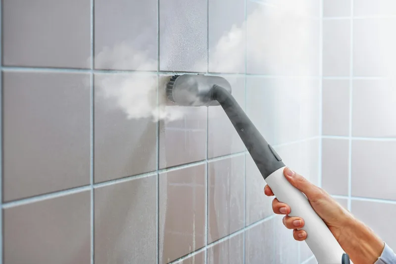 A steam cleaner sanitizing a tiled bathroom wall