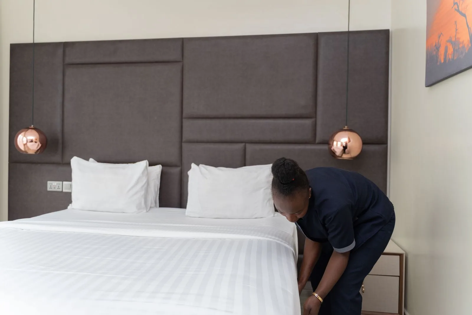 A housekeeper in a navy uniform making a bed with fresh white linens