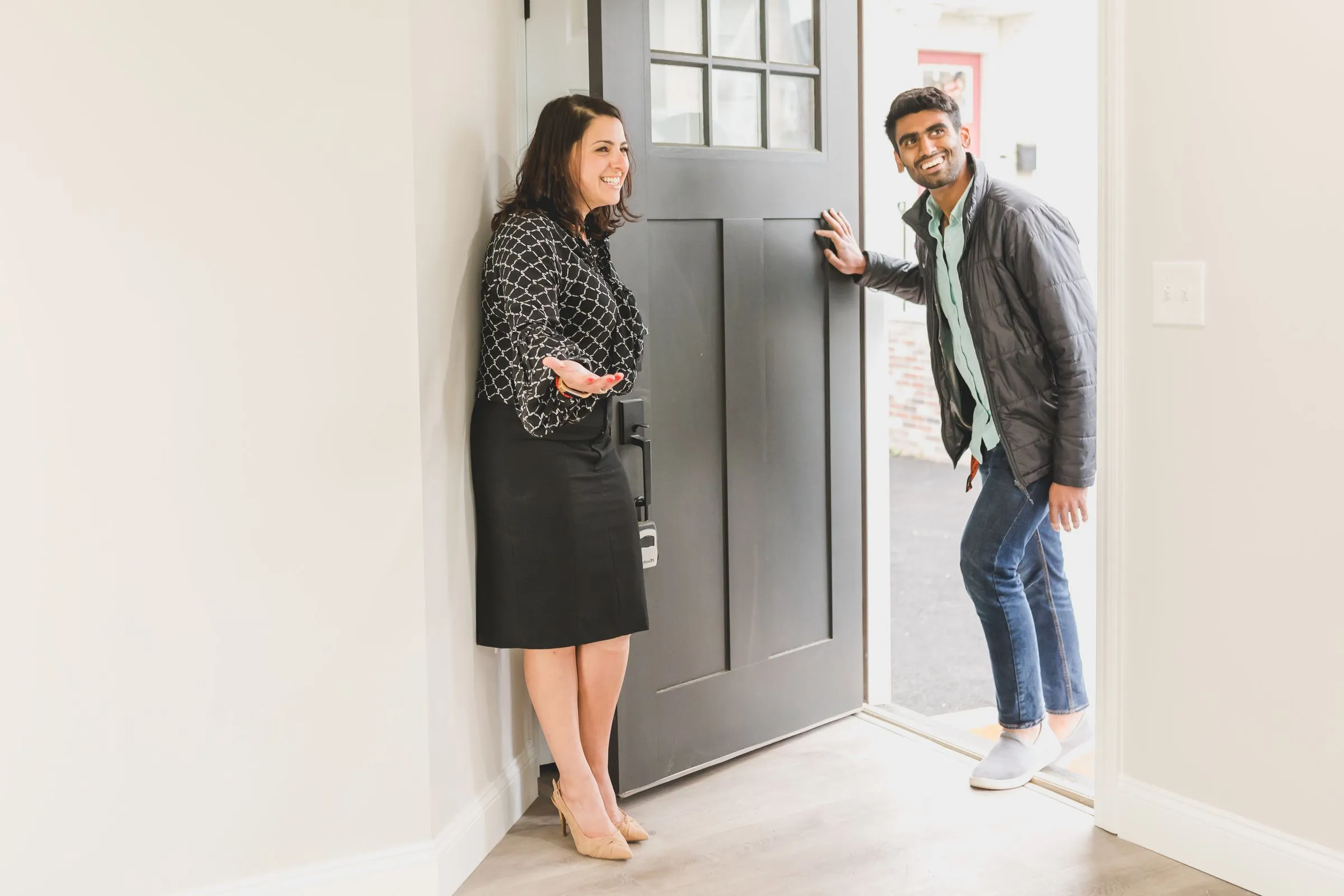 A smiling host welcoming a guest through the front door of a bright apartment